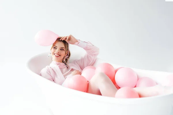 Happy young woman lying in bathtub and holding pink air balloon on white — Stock Photo