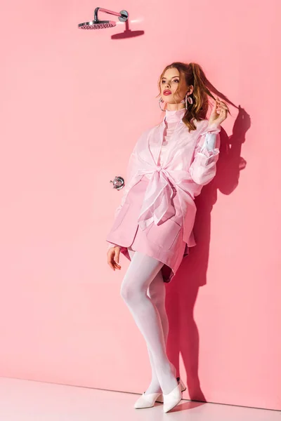 Attractive girl standing and touching hair on pink — Stock Photo