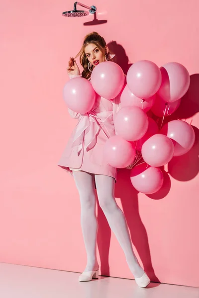 Hermosa mujer joven sosteniendo globos de aire mientras toca el pelo en rosa - foto de stock