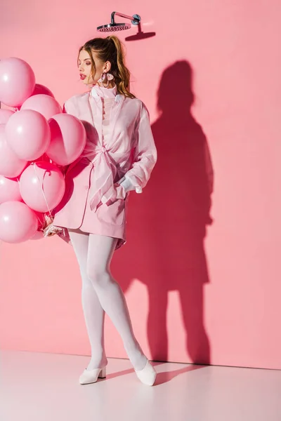 Beautiful young woman holding air balloons while standing with hand in pocket on pink — Stock Photo