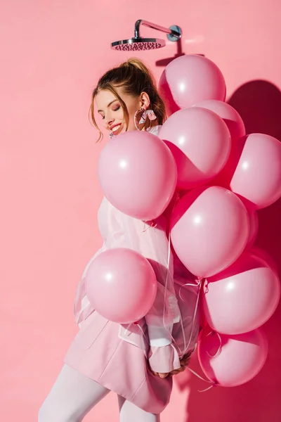 Счастливая красивая молодая женщина, держа воздушные шары, стоя на розовом — стоковое фото