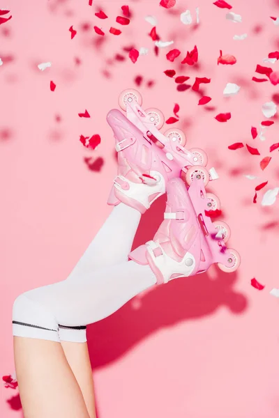 Обрезанный вид девушки в длинных носках и роликовых коньках возле лепестков роз на розовом — стоковое фото