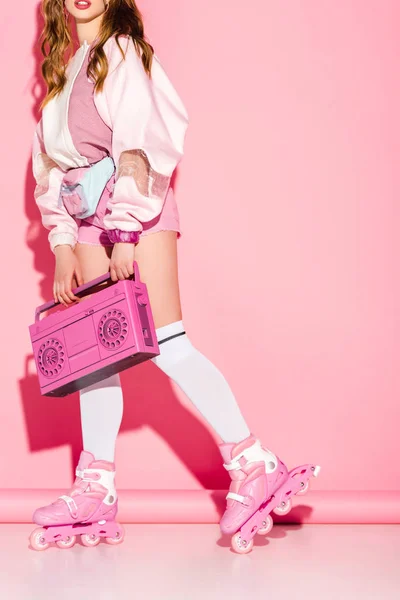 Обрезанный вид стильной девушки, держащей ретро-бумбокс, стоя в роликовых коньках на розовом — стоковое фото