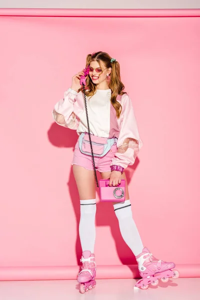 Щаслива стильна дівчина в сонцезахисних окулярах говорить на ретро телефоні на рожевому — стокове фото