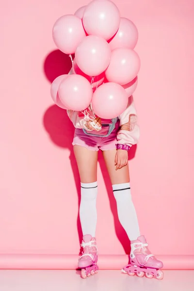 Женщина покрывает лицо воздушными шарами, стоя в роликовых коньках на розовом — стоковое фото