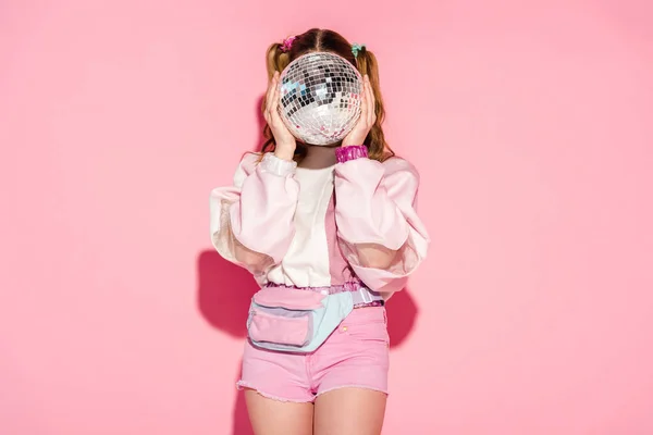 Girl covering face with shiny disco ball while standing on pink — Stock Photo