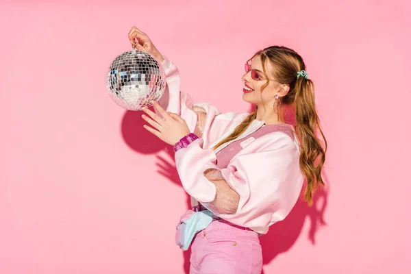 Jovem alegre olhando para bola de discoteca em rosa — Fotografia de Stock