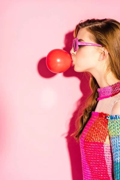 Chica atractiva en gafas de sol que sopla goma de mascar roja en rosa - foto de stock