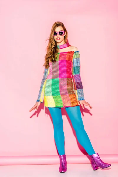 Hermosa mujer joven en gafas de sol de pie en vestido a cuadros en rosa - foto de stock