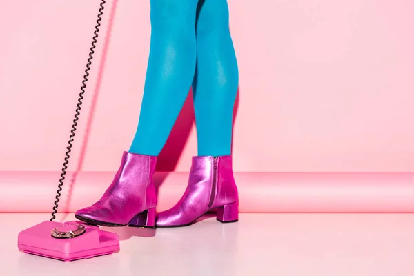 Vista cortada de jovem mulher em meias azuis perto de telefone retro em rosa — Fotografia de Stock