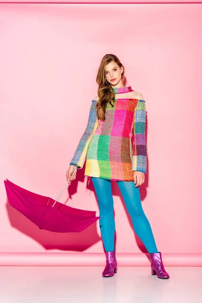 Beautiful young woman in plaid dress standing with umbrella on pink — Stock Photo