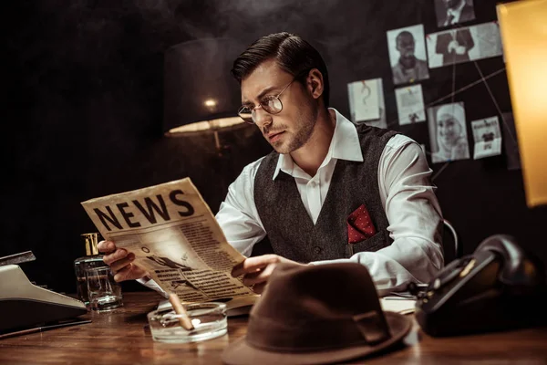 Konzentrierter Detektiv mit Brille liest Zeitung im dunklen Büro — Stockfoto