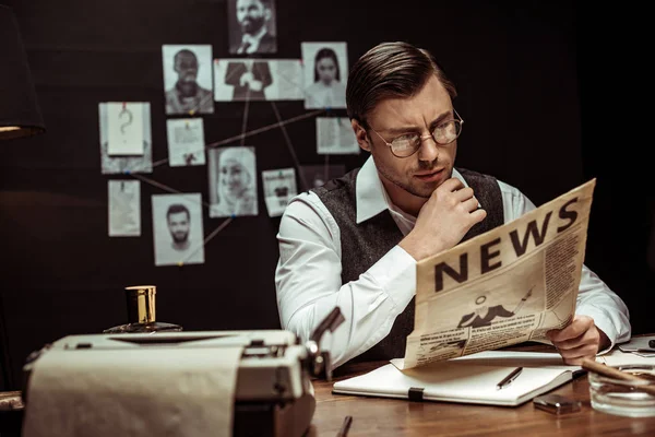 Концентрированный детектив в очках читает газету в темном кабинете — стоковое фото