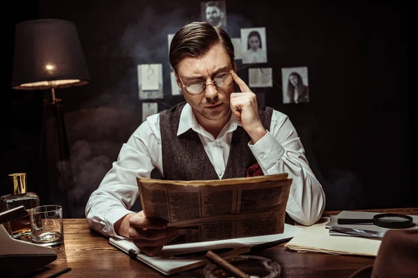 Konzentrierter Detektiv mit Brille liest Zeitung im dunklen Büro — Stockfoto