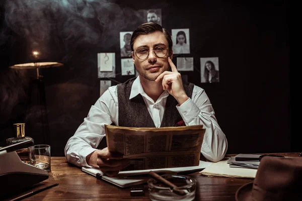 Концентрований детектив в окулярах читає газету в темному офісі — стокове фото