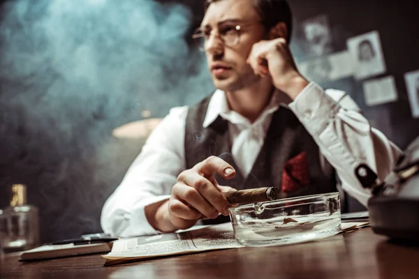 Selective focus of pensive detective in glasses holding cigar in office — Stock Photo