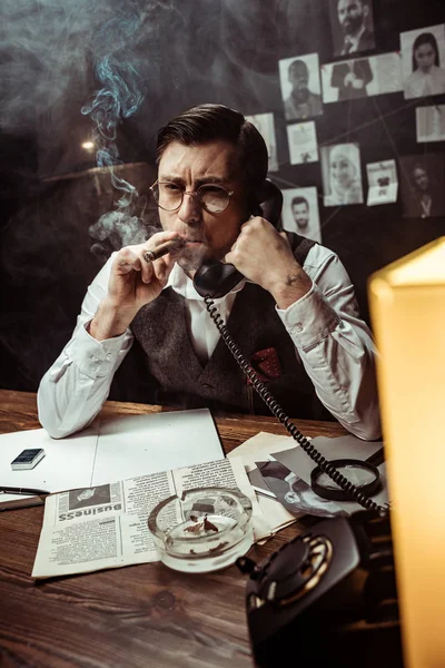 Pensive detective in glasses talking on telephone in dark office — Stock Photo