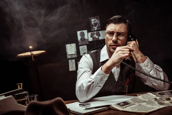 Pensive detective in glasses talking on telephone in dark office — Stock Photo