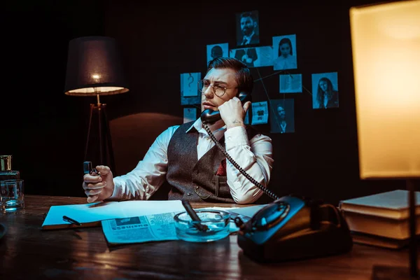 Pensive detective in glasses talking on telephone in dark office — Stock Photo