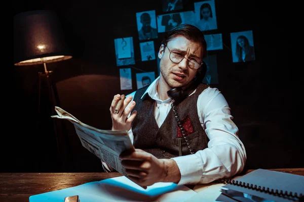 Concentrated detective in glasses holding newspaper and talking on telephone — Stock Photo
