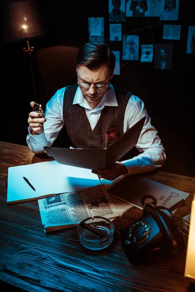 Vista ad alto angolo di detective concentrato in occhiali lettura fascicolo in ufficio scuro — Foto stock