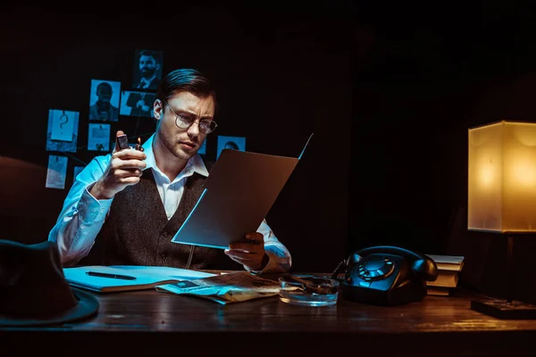 Concentrated detective in glasses reading dossier in dark office — Stock Photo