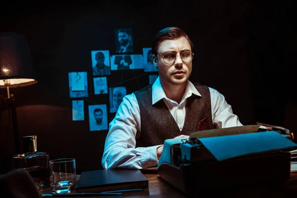 Concentrated detective in glasses using typewriter in dark office — Stock Photo