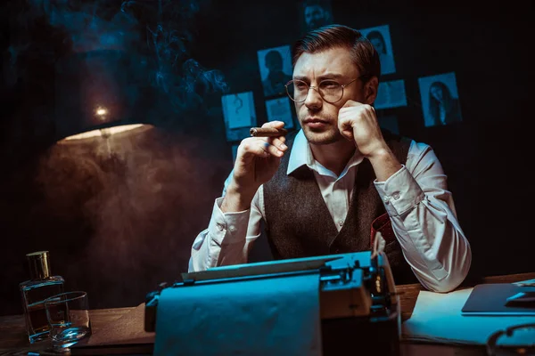 Pensive detective in glasses holding cigar and looking away in dark office — Stock Photo