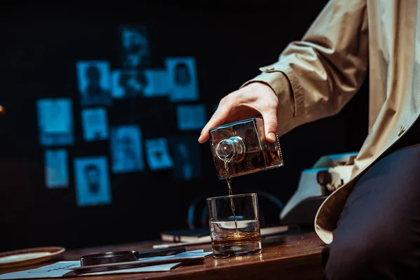 Partial view of detective pouring cognac in glass while sitting on table — Stock Photo