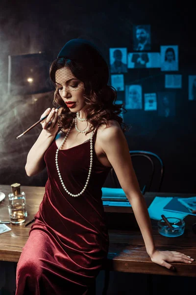 Woman in dress sitting on table and holding mouthpiece in dark office — Stock Photo