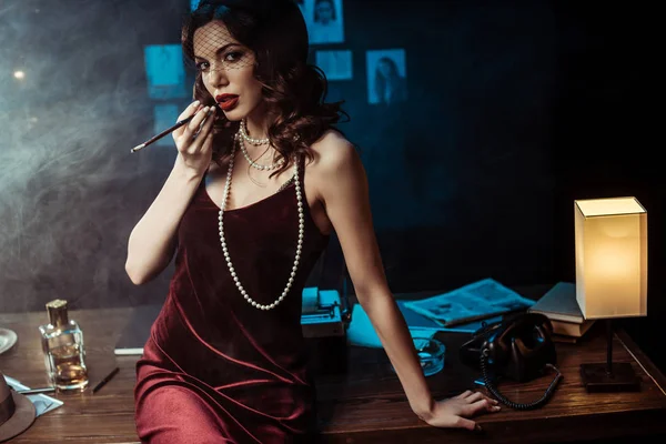Frau im Kleid sitzt auf Tisch und hält Mundstück im dunklen Büro — Stockfoto