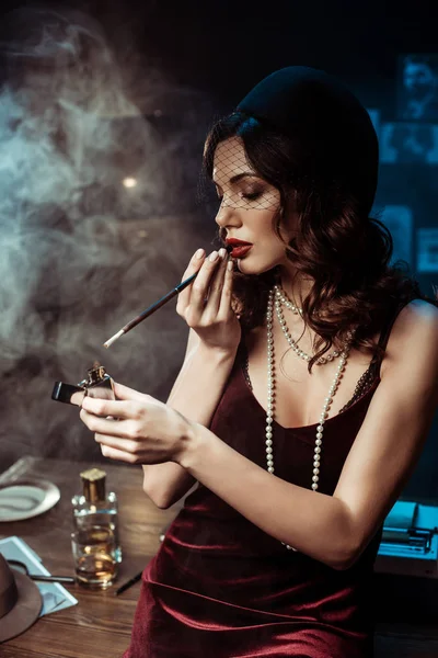 Hermosa mujer con la boquilla de iluminación cigarrillo con encendedor en la oficina oscura - foto de stock