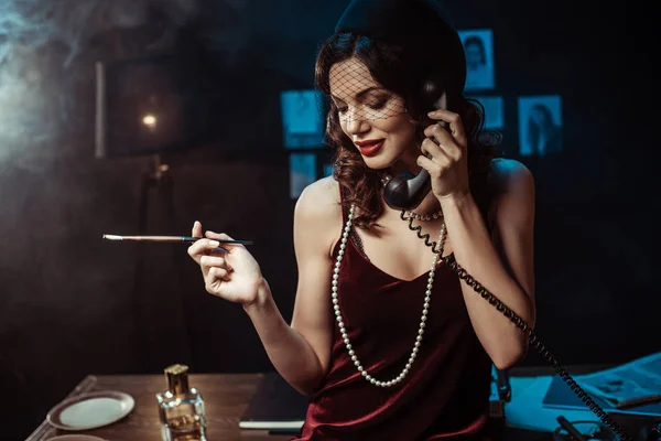 Attractive woman with mouthpiece talking on telephone in dark office — Stock Photo