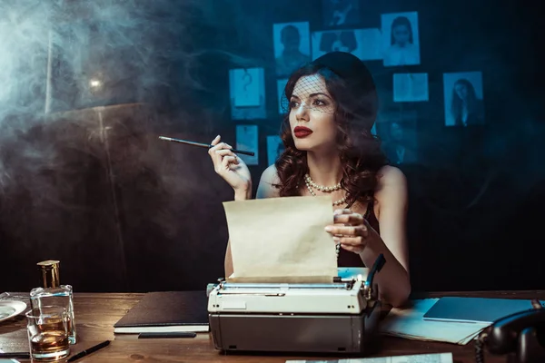 Nachdenkliche Frau mit Mundstück auf Schreibmaschine im dunklen Büro — Stockfoto