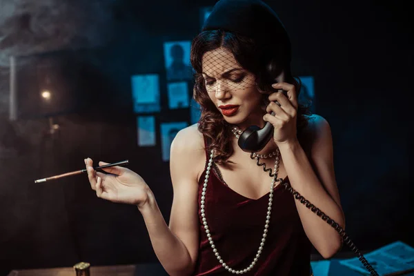 Mujer atractiva triste con la boquilla hablando por teléfono en la oficina oscura - foto de stock
