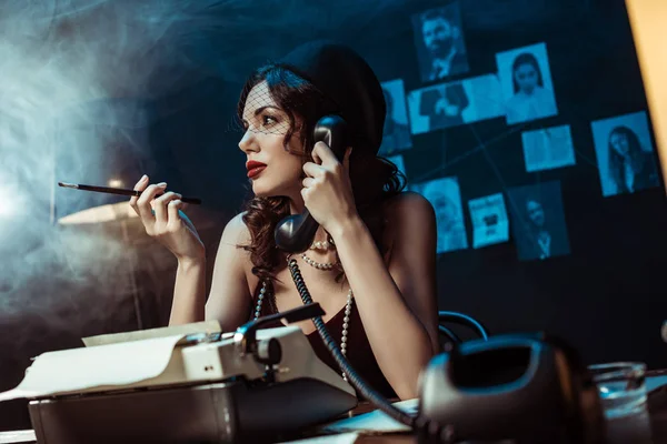 Belle femme avec embout buccal parlant au téléphone dans un bureau sombre — Photo de stock