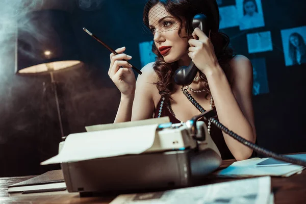Attractive woman with mouthpiece talking on telephone in dark office — Stock Photo