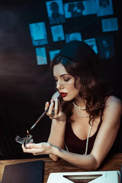 Beautiful woman with mouthpiece lighting cigarette with lighter in dark office — Stock Photo