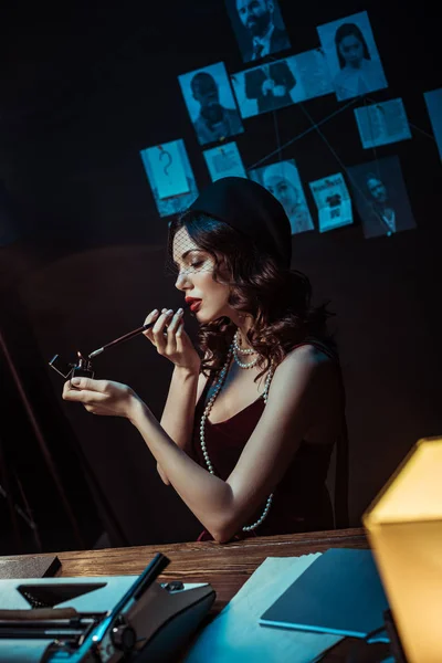 Beautiful woman with mouthpiece lighting cigarette in dark office — Stock Photo