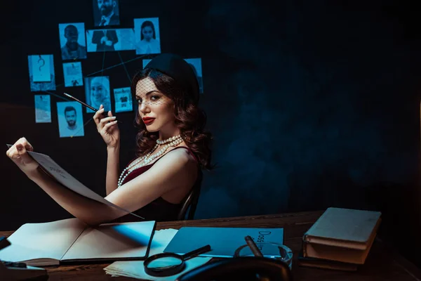 Ernsthafte Frau mit Mundstück, das Dossier hält und in dunkle Büros in die Kamera blickt — Stockfoto