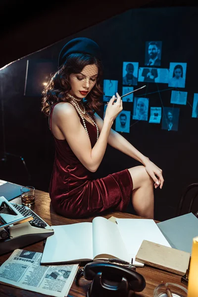 Pensive woman in dress and fascinator hat holding mouthpiece and looking at documents in dark office — Stock Photo