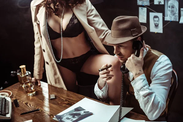 Sexy woman in black lingerie and trench coat seducing detective in dark office — Stock Photo