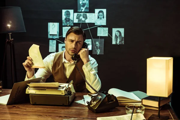 Detective holding document while talking on telephone in office — Stock Photo