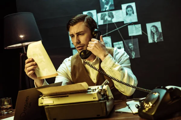 Detective reading document while talking on telephone in office — Stock Photo