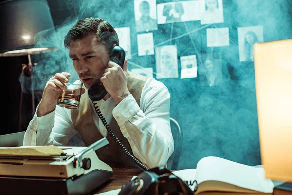Detective che parla al telefono e beve cognac in ufficio — Foto stock