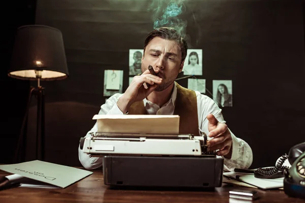 Detective smoking cigar and using typewriter in dark office — Stock Photo