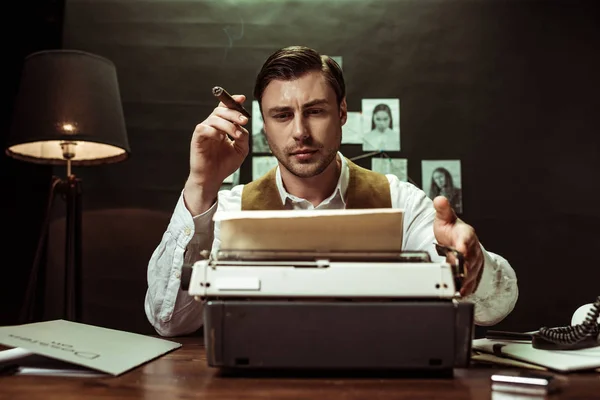 Detetive sério com charuto usando máquina de escrever no escritório escuro — Fotografia de Stock