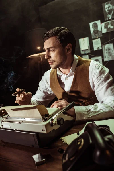 Detective sosteniendo cigarro mientras usa la máquina de escribir en la oficina oscura - foto de stock