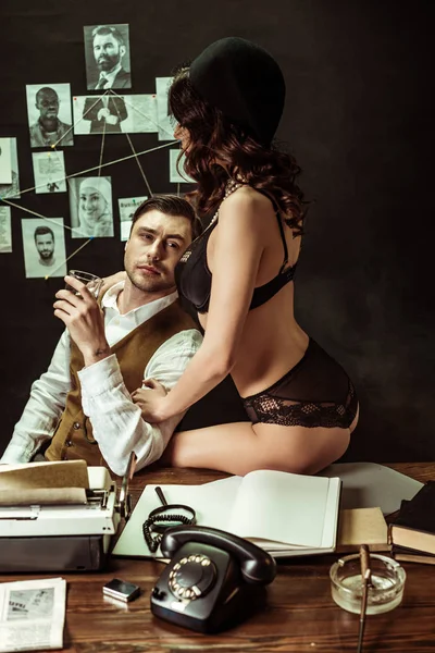 Sexy girl in black lingerie seducing detective in dark office — Stock Photo