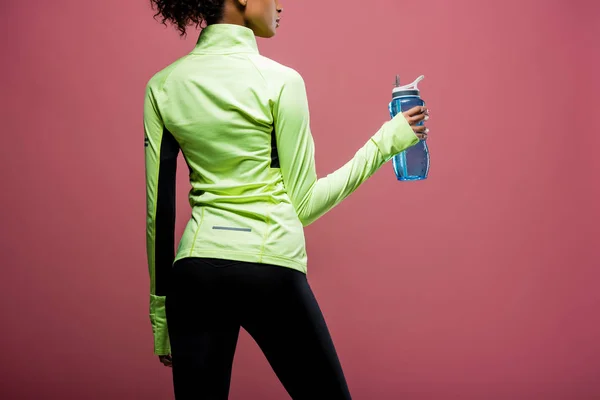 Back view of african american sportswoman in track jacket with sport bottle isolated on brown — Stock Photo